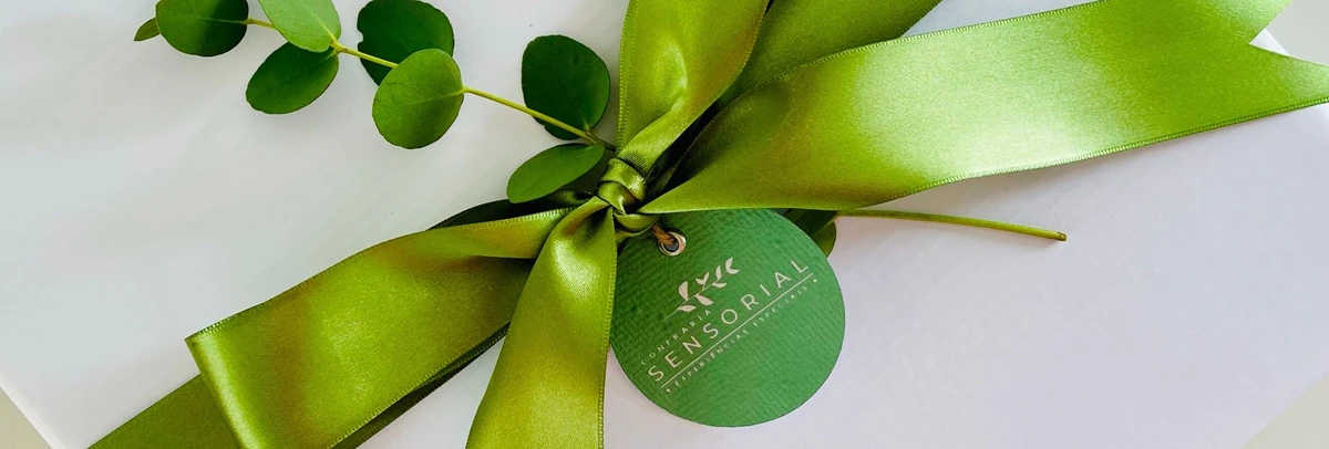 Presente da Confraria Sensorial com laço verde, folhagem e etiqueta da marca.